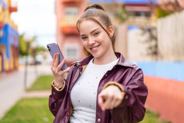 Mladá Hezká Dívka Používající Mobilní Telefon Venku Ukazuje Prstem Vás — Stock fotografie