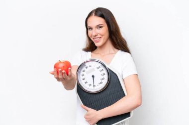 Beyaz arka planda izole edilmiş beyaz bir kadın elinde tartı makinesiyle bir elma sunuyor.
