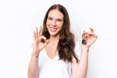 Beyaz arka planda izole edilmiş ev anahtarlarını tutan beyaz kadın parmaklarıyla tamam işareti gösteriyor.