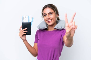 Şişirilebilir Seyahat Yastığı ile genç ve güzel Uruguaylı kadın beyaz arka planda izole edilmiş gülümseyerek zafer işareti gösteriyor.