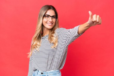 Genç Uruguaylı kadın kırmızı arka planda izole edilmiş bir şekilde baş parmak işareti yapıyor.