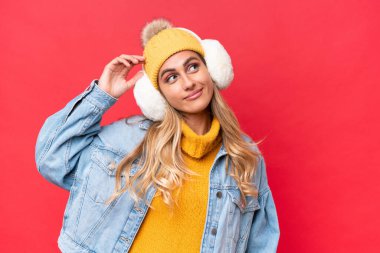 Genç, güzel Uruguaylı kadın, kırmızı arka planda izole edilmiş kışlık kuklalar takıyor, kuşkuları var ve kafası karışmış bir halde.