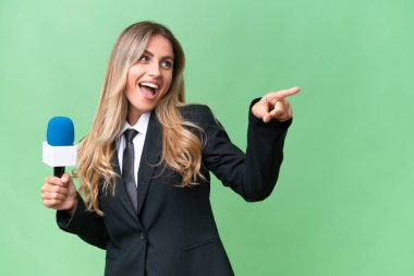 Genç, güzel Uruguaylı bir televizyon sunucusu, izole edilmiş arka planda parmak göstererek bir ürün sunuyor.