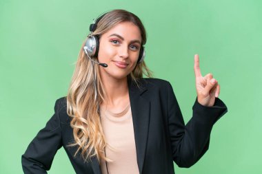 Tele pazarlamacı güzel Uruguaylı kadın izole edilmiş arka planda kulaklıkla çalışıyor ve en iyinin işaretini veriyor.