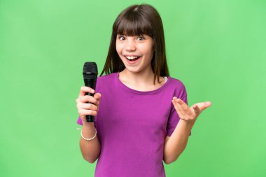 Küçük şarkıcı kız, izole edilmiş bir arka planda şok olmuş bir yüz ifadesiyle mikrofonu eline aldı.