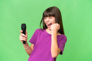 Küçük şarkıcı kız izole bir arka planda mikrofonu eline aldı ve zaferi kutladı.