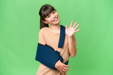 Kırık kollu beyaz bir kız ve izole edilmiş arka planda askısı var. Parmaklarıyla beşi sayıyor.