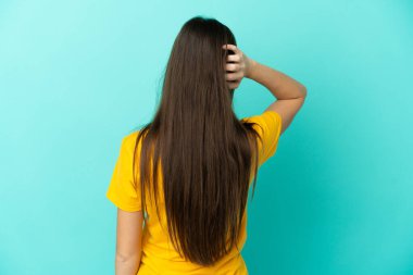 Kafkasyalı genç bir kadın mavi arka planda izole edilmiş ve düşünüyor.