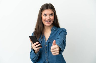 Young caucasian woman isolated on white background using mobile phone while doing thumbs up