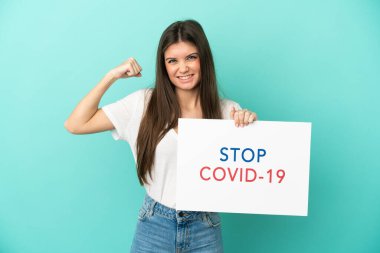 Beyaz bir kadın mavi arka planda izole edilmiş. Elinde yazılı bir levha var. Covid 19 'u durdur ve güçlü bir hareket yap.