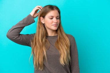 Genç sarışın kadın, mavi arka planda izole edilmiş. Kafasını kaşırken şüpheleri var.