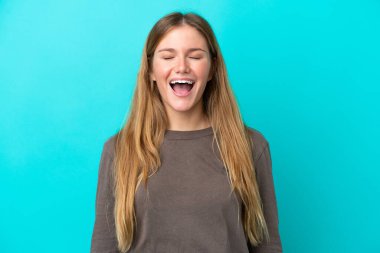 Mavi arka planda izole edilmiş genç sarışın kadın ağzı açık bağırıyor.