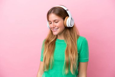 Pembe arka planda izole edilmiş genç sarışın kadın müzik dinliyor.