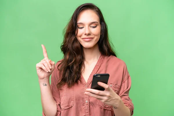 Young Caucasian Woman Isolated Background Using Mobile Phone Lifting Finger — Stock Photo, Image