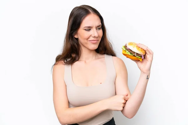Młoda Kaukaska Kobieta Trzyma Hamburgera Białym Tle Smutnym Wyrazem Twarzy — Zdjęcie stockowe
