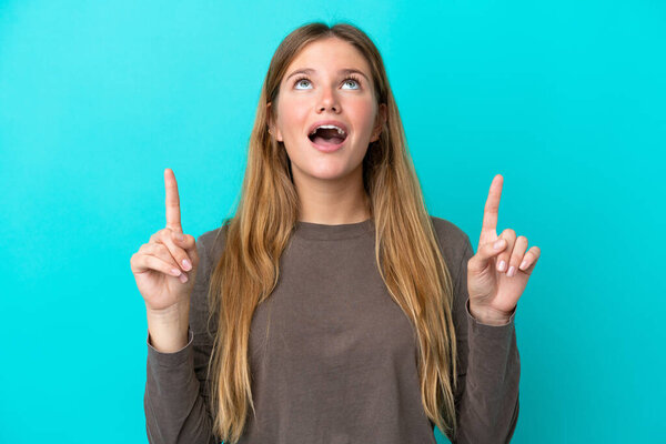 Young blonde woman isolated on blue background surprised and pointing up