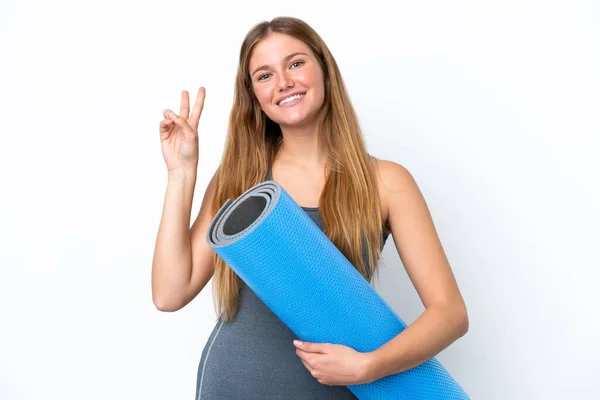年轻的女运动员一边带着垫子一边笑着去上瑜伽课 并展示胜利的标志 — 图库照片