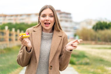 Sarışın, güzel bir kadın açık havada tart tutuyor. Şaşırmış ve parmağıyla işaret ediyor.