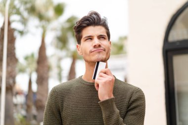 Açık havada elinde kredi kartı olan genç beyaz bir adam...