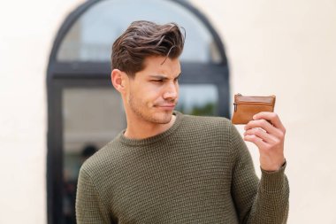 Kafkasyalı genç bir adam dışarıda üzgün bir ifadeyle bir cüzdan tutuyor.
