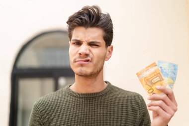 Kafkasyalı genç adam üzgün bir ifadeyle dışarıda çok para alıyor.