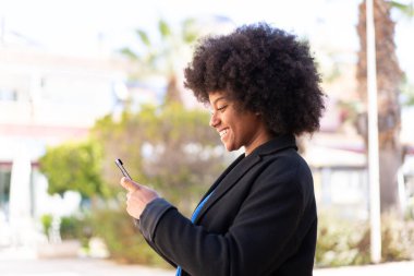 Dışarıdaki Afrikalı Amerikalı kız cep telefonuyla mesaj ya da e-posta yolluyor.