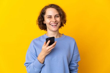 Pembe arka planda cep telefonu kullanan genç bir İngiliz kadın.