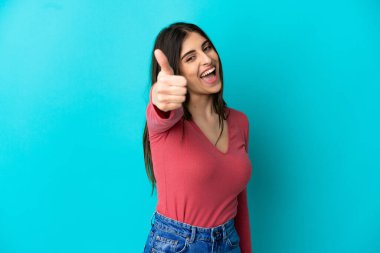 Genç beyaz kadın mavi arka planda izole edildi. Başparmakları havada çünkü iyi bir şey oldu.