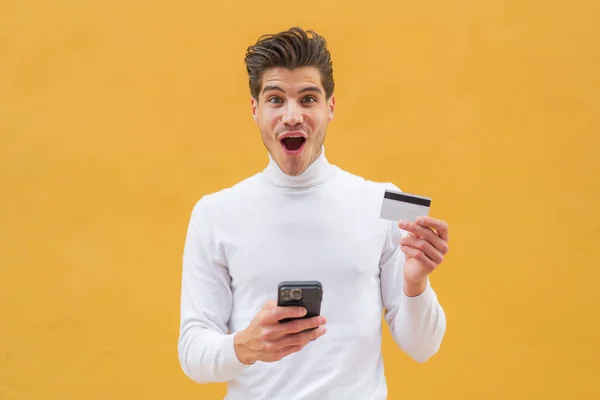 Mladý Běloch Venku Nakupuje Mobilem Drží Kreditní Kartu Překvapeným Výrazem — Stock fotografie