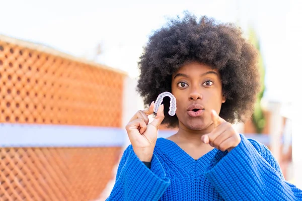 African American Girl Holding Invisible Braces Outdoors Surprised Pointing Front — Stock Photo, Image