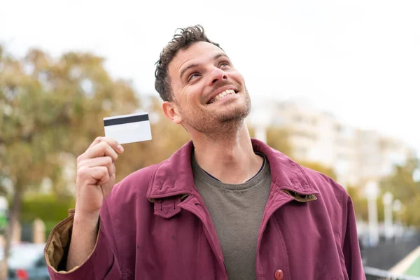 Young Caucasian Man Holding Credit Card Outdoors Looking While Smiling — Stock Photo, Image