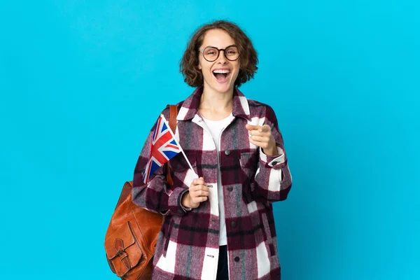 拿着英国国旗的英国年轻女子 蓝色背景孤立 惊讶地指着前方 — 图库照片
