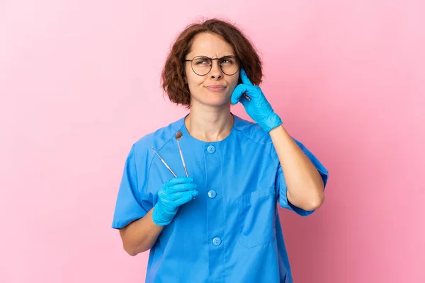 英国女牙医将工具放在粉红色背景下孤立的 有疑问和思考的地方 — 图库照片