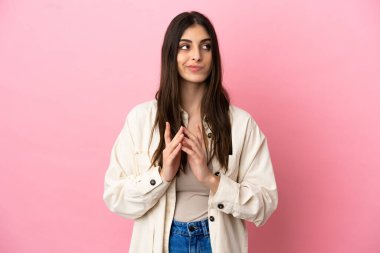 Pembe arka planda izole edilmiş genç beyaz kadın bir şeyler planlıyor.