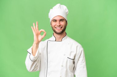 Genç, yakışıklı aşçı, izole edilmiş arka planda parmaklarıyla imza atıyor.