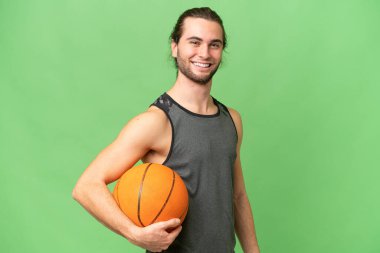 Genç yakışıklı adam yeşil krom arka planda izole edilmiş basketbol oynuyor.