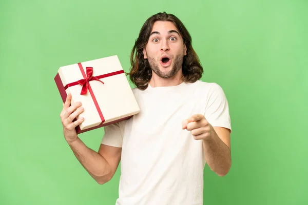 Young Handsome Man Holding Gift Isolated Background Surprised Pointing Front — Stock Photo, Image