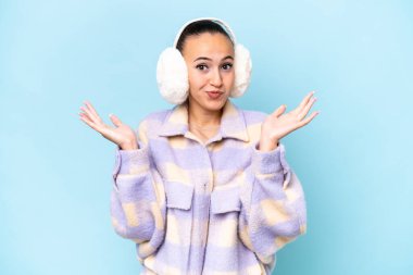 Mavi arka planda izole edilmiş kışlık kuklalar giyen genç bir Arap kadının el kaldırırken şüpheleri var.