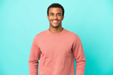 Afro-Amerikalı yakışıklı adam mavi arka planda gülüyor.