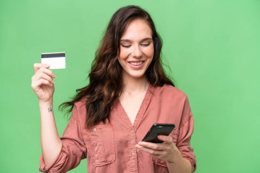 Young caucasian woman over isolated background buying with the mobile with a credit card
