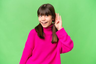 İzole edilmiş arka planda küçük beyaz bir kız. Kulağına elini sürerek bir şeyler dinliyor.