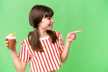 İzole edilmiş arka planda çikolatalı milkshake 'i olan genç adam bir ürünü sunmak için kenarı işaret ediyor.