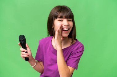 Küçük şarkıcı kız izole edilmiş bir arka planda mikrofonu eline alıp bir şeyler fısıldıyor.