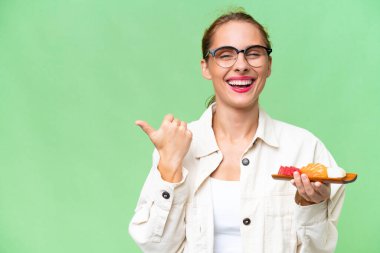 Young caucasian woman holding sashimi over isolated background pointing to the side to present a product