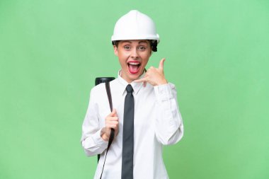 Miğferli genç bir mimar kadın izole edilmiş arka plan üzerinde planları tutuyor ve telefon jesti yapıyor. Bana geri dönüş işareti ver.