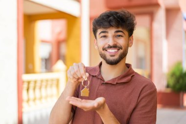 Genç Arap yakışıklı adam evin anahtarlarını tutarken neşeli bir ifade takındı.