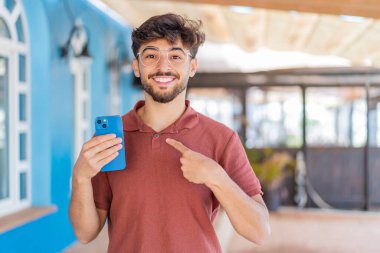 Genç Arap yakışıklı adam dışarıda cep telefonu kullanıyor ve yüzünde sürpriz bir ifade var.