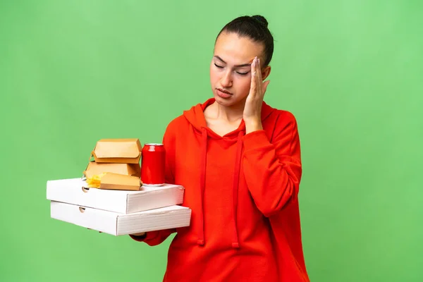 Junge Araberin Hält Fast Food Vor Isoliertem Hintergrund Mit Kopfschmerzen — Stockfoto