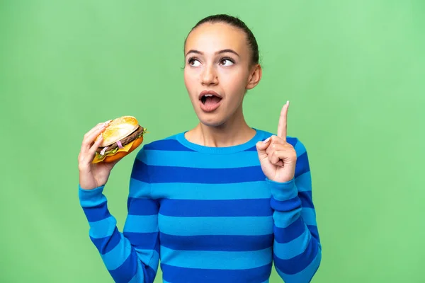 Młoda Arabka Trzymająca Hamburgera Nad Odosobnionym Tłem Myśląc Wskazującym Palcem — Zdjęcie stockowe
