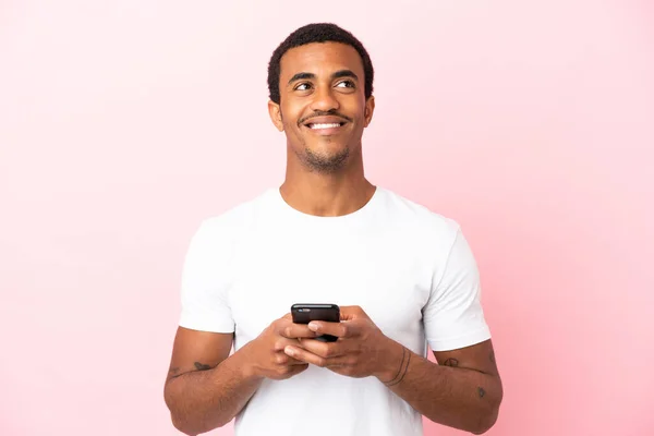 Afroamerykanin Przystojny Mężczyzna Odizolowanym Różowym Tle Pomocą Telefonu Komórkowego Patrząc — Zdjęcie stockowe